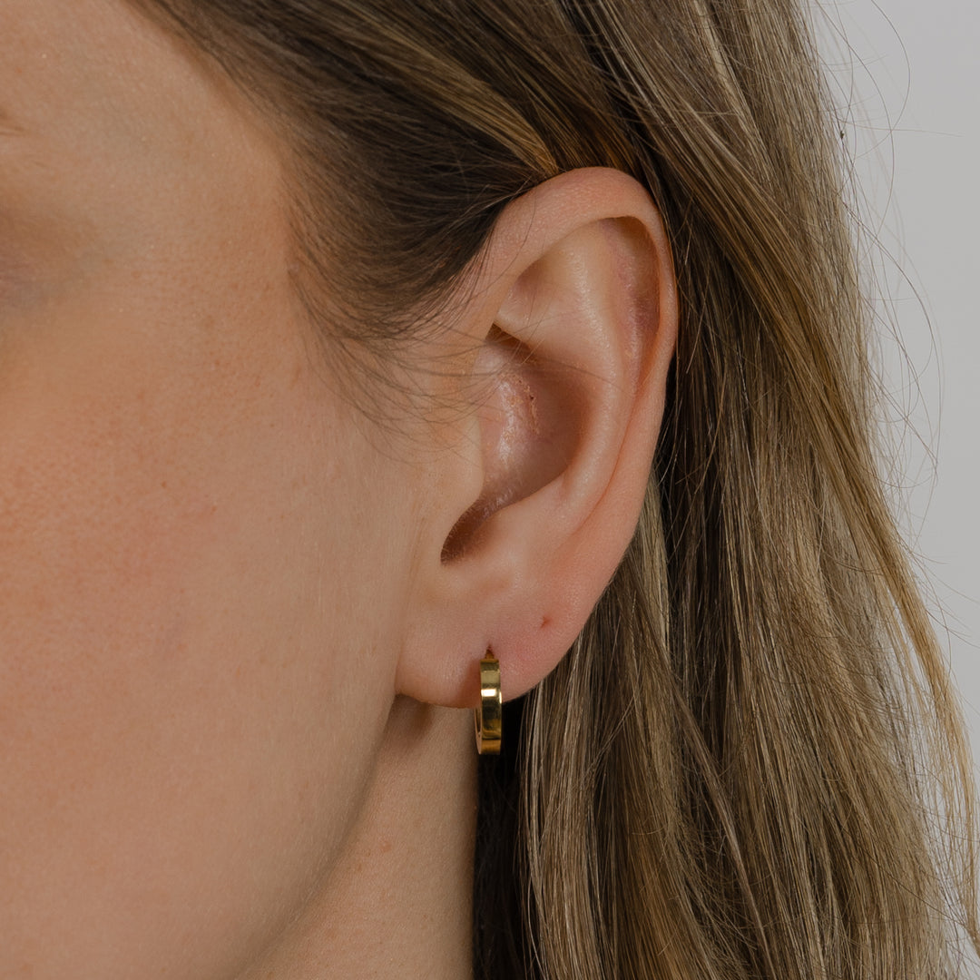 Close-up of an ear wearing a gold hoop earring with a neutral background