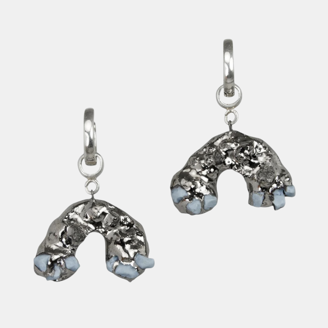 Sidabrinių auskarų pora su mėlynais akcentais šviesiai pilkame fone